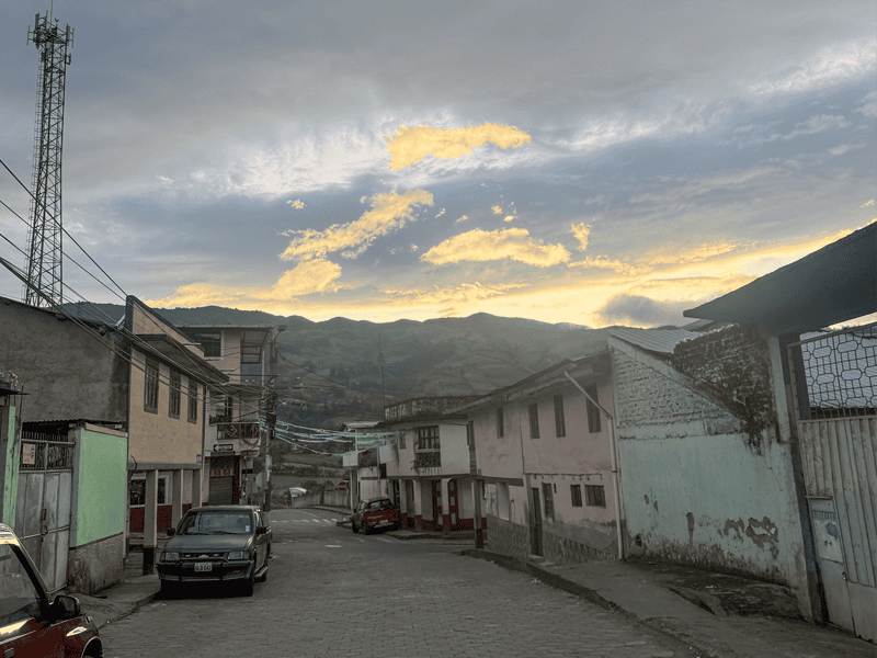 Town at Sunset A small town in rural Ecuador at sunset, with homes lining a quiet street and mountains rising in the background beneath a dramatic sky.